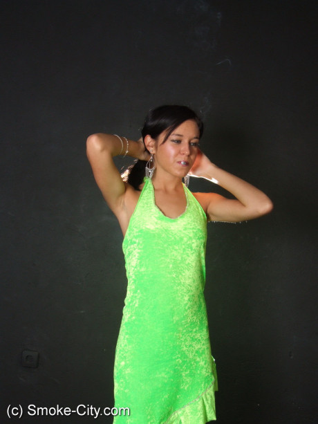 Dark haired young wears a lime dress and pointy heels while smoking