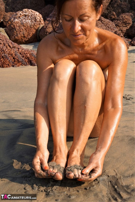 Naked cougar girl Diana Ananta covers her feet in beach sand at low tide - #1145666