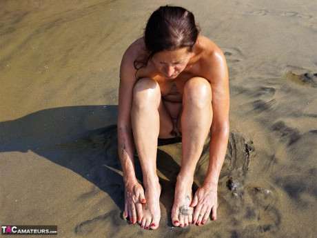 Naked cougar girl Diana Ananta covers her feet in beach sand at low tide - #1145670