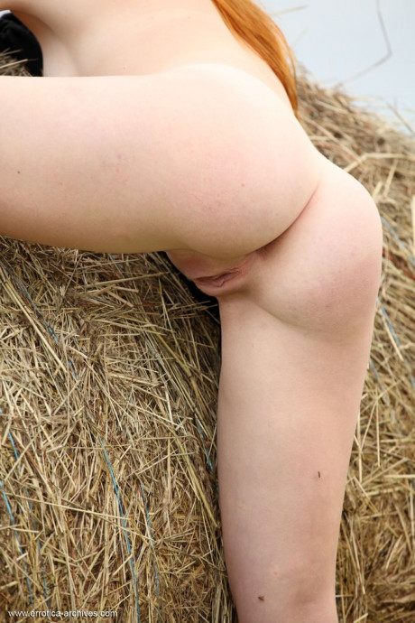 Redheaded young Amber A gets totally nude against a round bale in a field - #869941