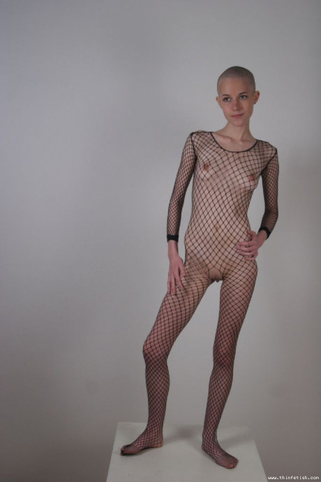 Solo model with a shaved head poses in a fishnet bodystocking