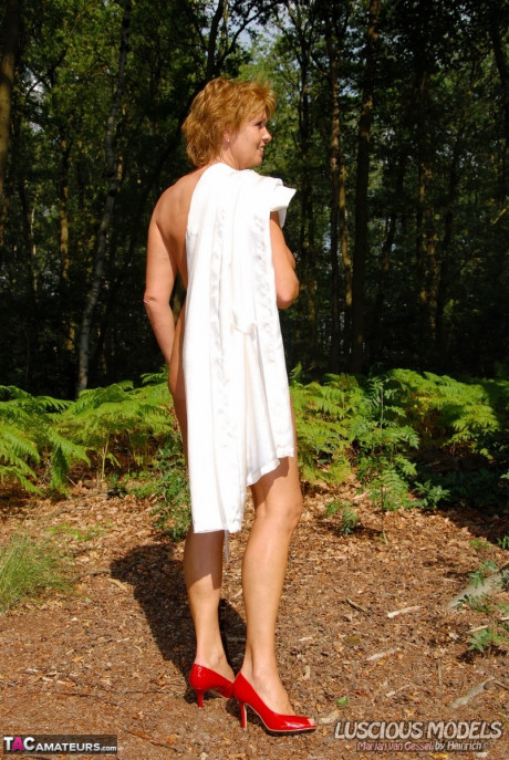 Mature ginger head removes a robe to stand naked in red heels while in the woods - #1087766