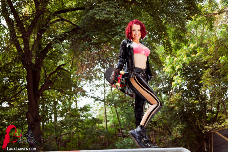 Redheaded model Lara Larsen unzips her latex clothing at a skate park