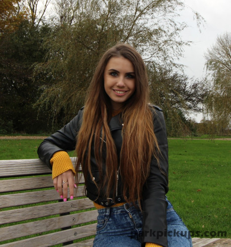 Long-haired young in a leather jacket puts a hard meat in her mouth in a park - #818988