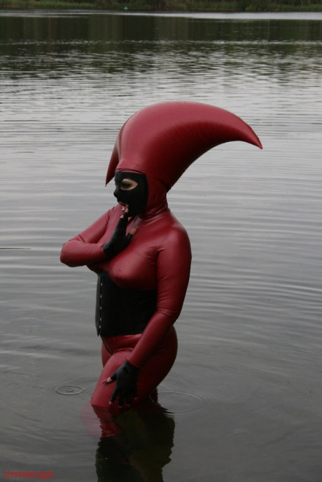 Fetish model Avengelique wades into a body of water in a rubber costume